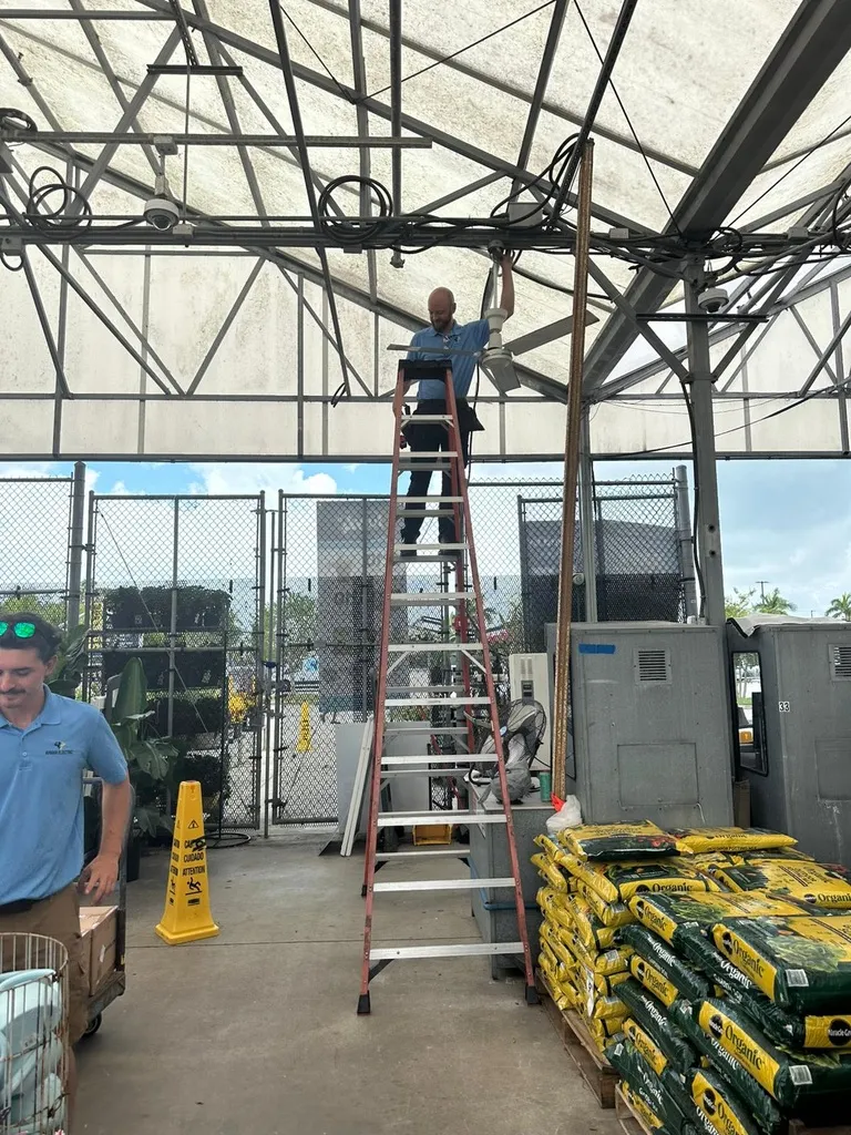 A man on a ladder adjusting electric cables on a ceiling fan.